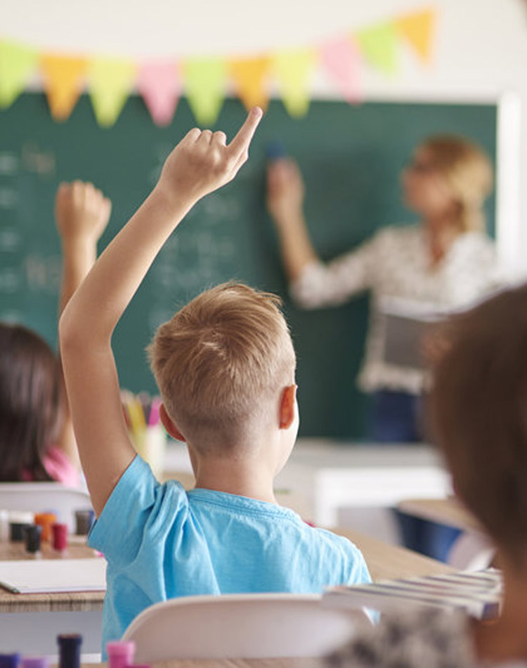 Teacher pointing to a chalkboard as students raise their hands