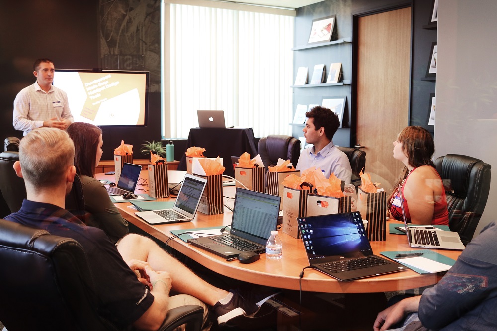 A standing person presenting to people sitting around a conference room table