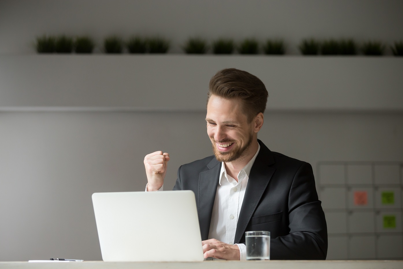 Person sitting at a laptop smiling and clenching his fist