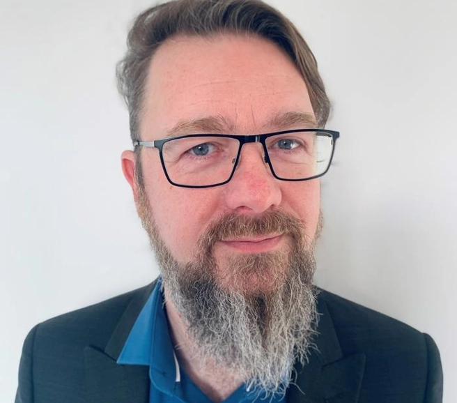 Phil: Headshot of a smiling man. He has a beard and is wearing glasses